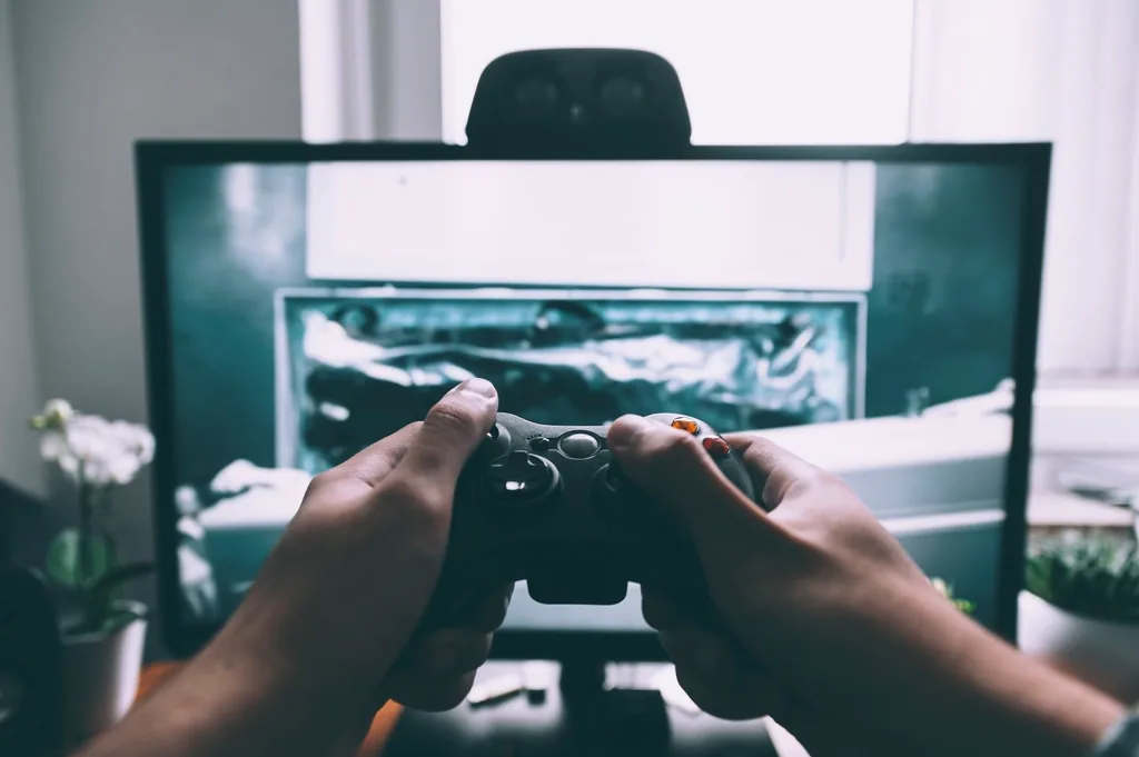 Hands holding a game controller in front of a monitor